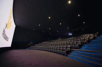 Salle de cinéma vide avec des rangées de sièges rouges et un éclairage tamisé sur les murs.