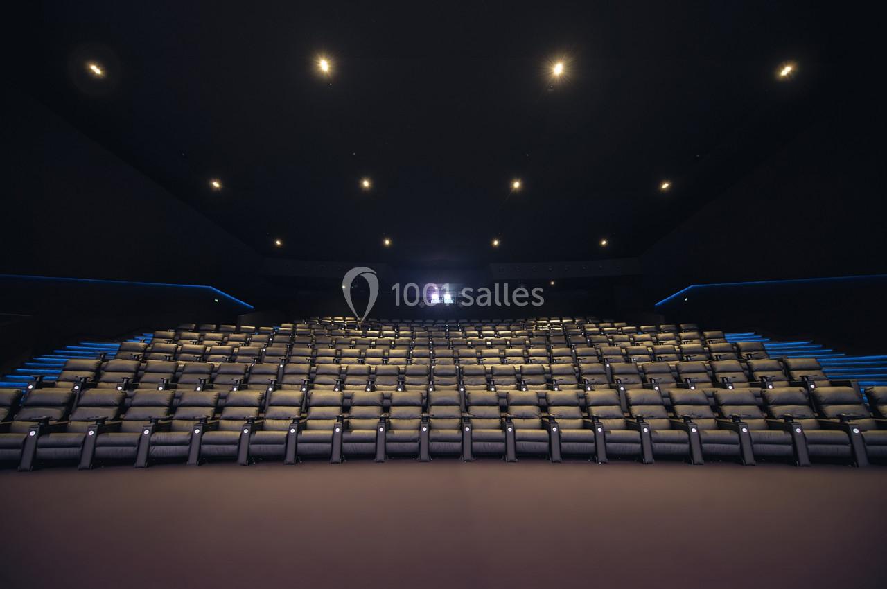 Salle de cinéma vide avec des rangées de sièges en cuir beige, éclairée par des lumières tamisées au plafond.