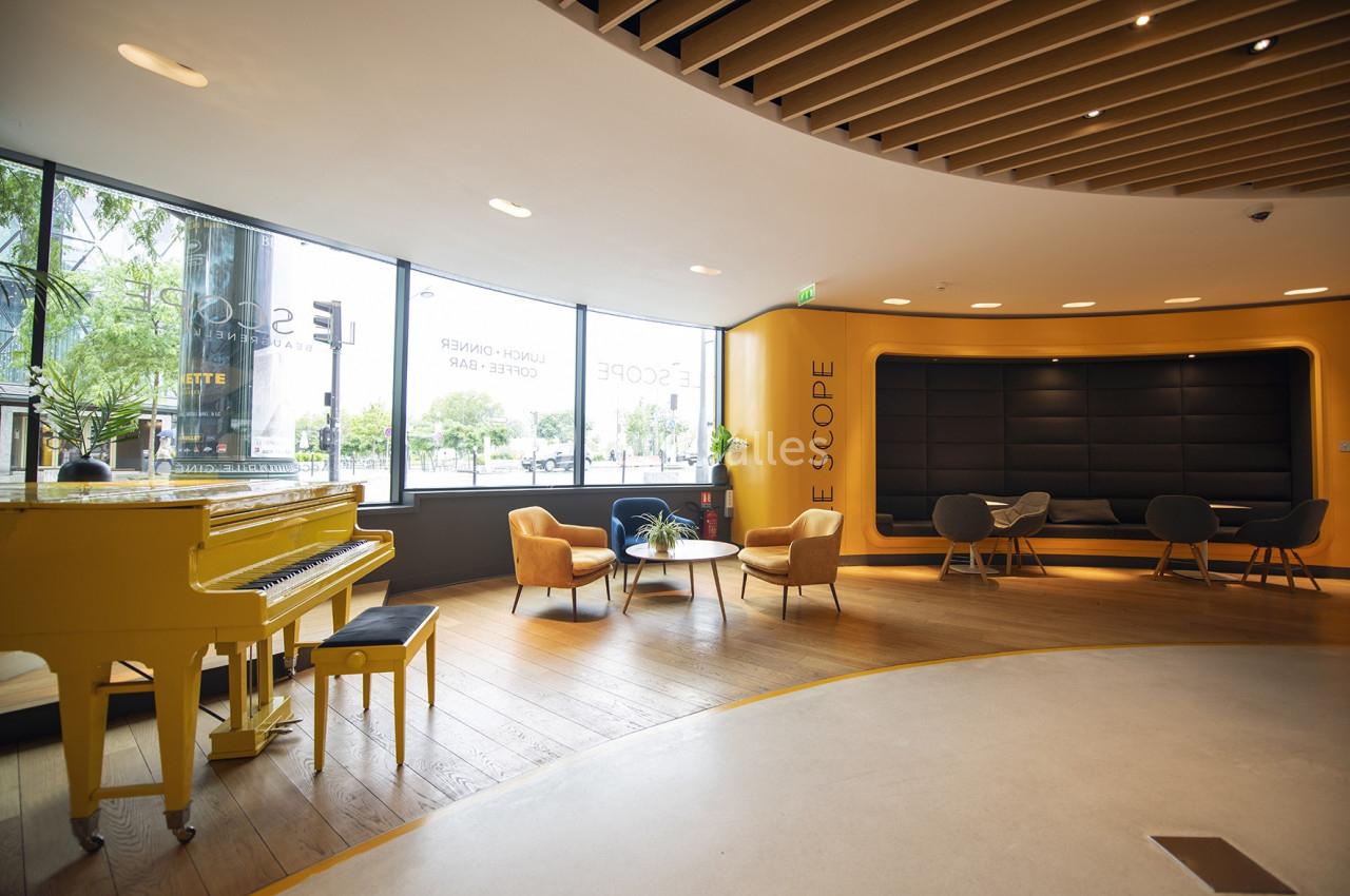 Espace lumineux avec un piano jaune, des fauteuils modernes et une grande baie vitrée donnant sur l'extérieur.