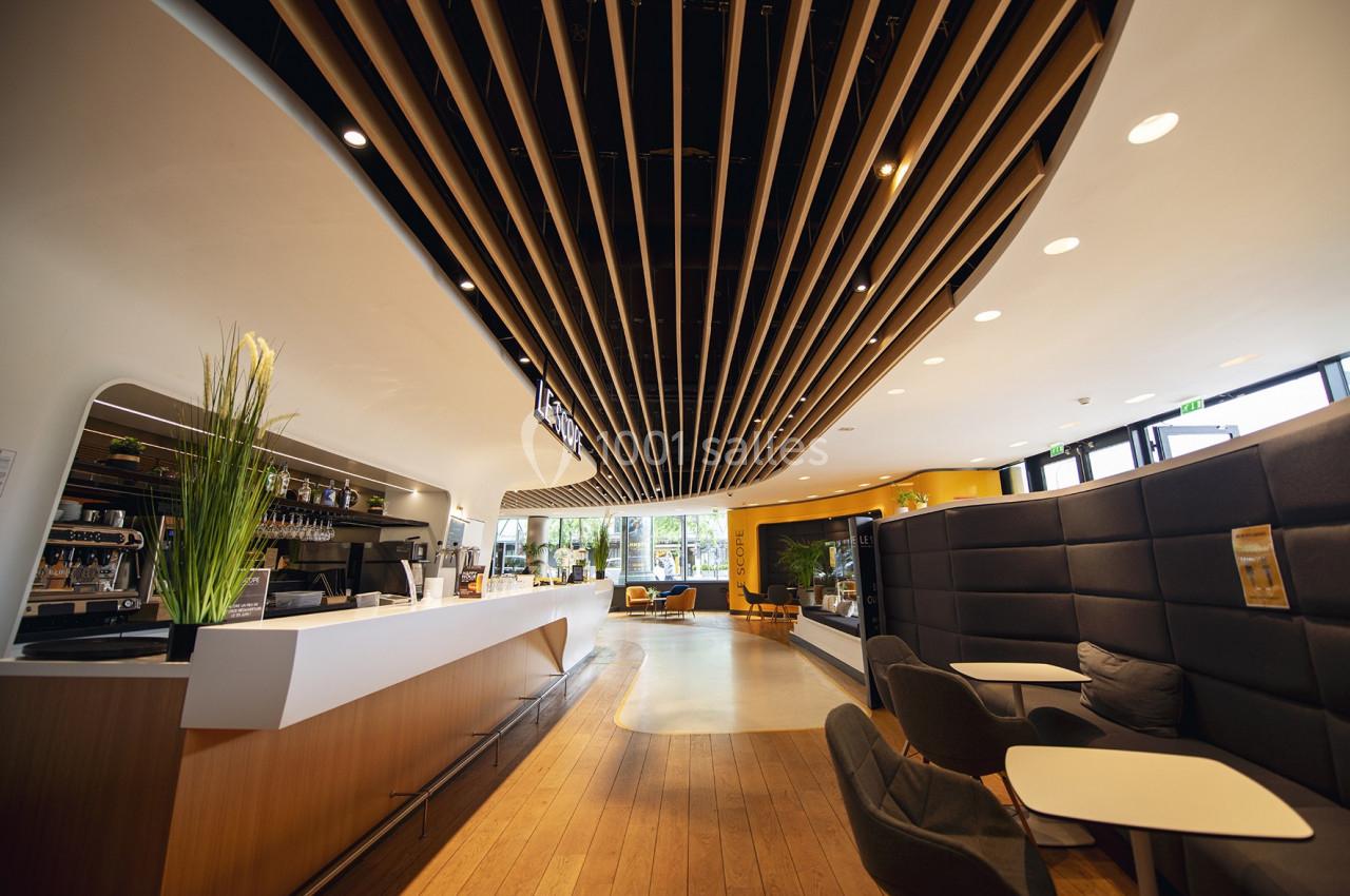 Intérieur d'un café moderne avec un comptoir, des sièges confortables et un plafond en bois ondulé.