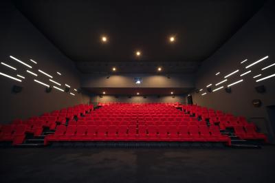 Salle de cinéma vide avec des rangées de sièges rouges et un éclairage tamisé sur les murs.