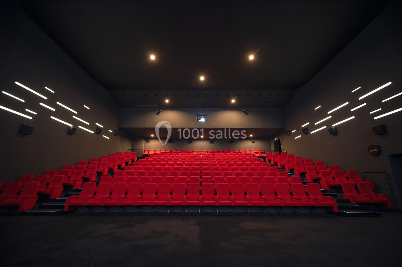 Salle de cinéma vide avec des rangées de sièges rouges et un éclairage tamisé au plafond.