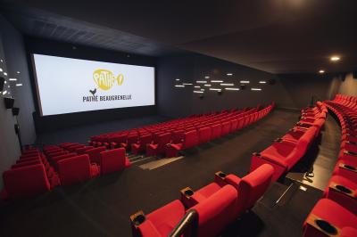Salle de cinéma vide avec des rangées de sièges rouges et un éclairage tamisé sur les murs.