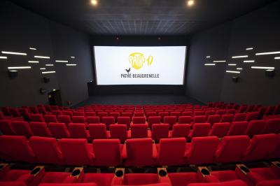 Salle de cinéma vide avec des rangées de sièges rouges et un éclairage tamisé sur les murs.