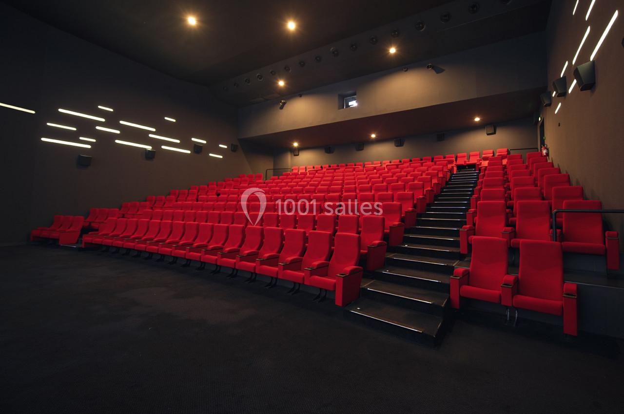 Salle de cinéma vide avec des rangées de sièges rouges et un éclairage tamisé sur les murs.