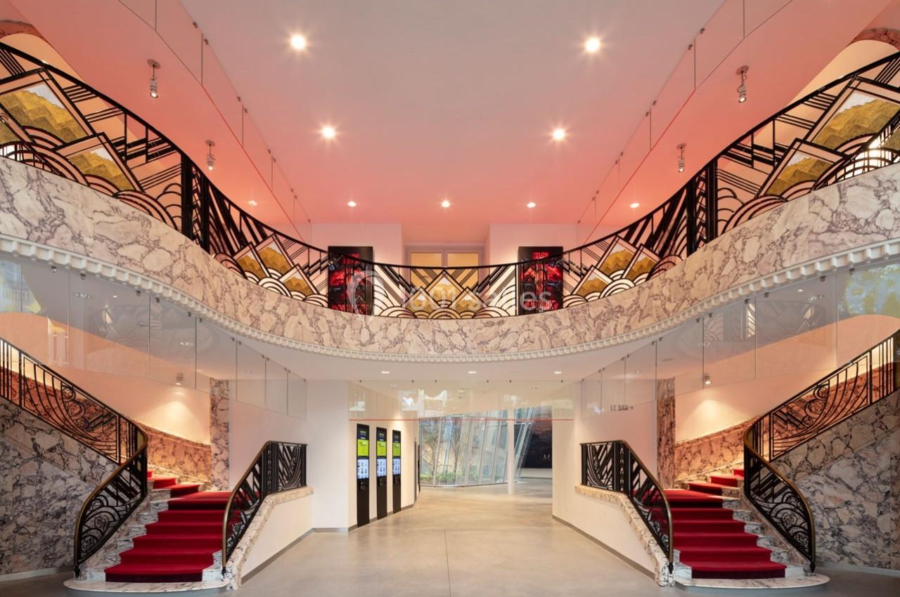 Location salle Paris 9 (Paris) - Pathé Palace  #2 Hall d'entrée avec escalier symétrique, tapis rouge, balustrades décorées et éclairage chaleureux.