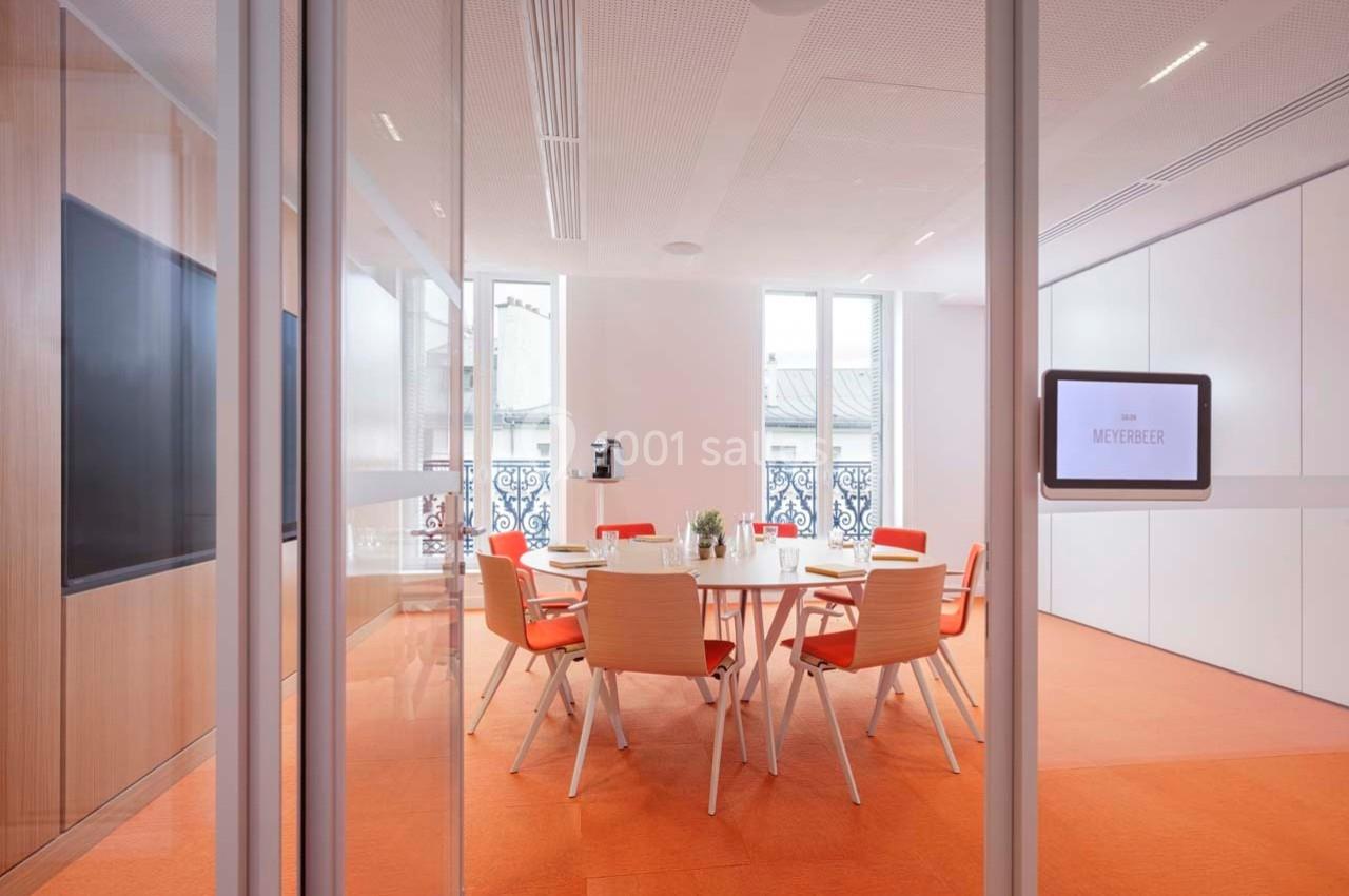 Location salle Paris 9 (Paris) - Pathé Palace  #5 Salle de réunion lumineuse avec table ronde, chaises orange et vue sur des fenêtres donnant sur des balcons.