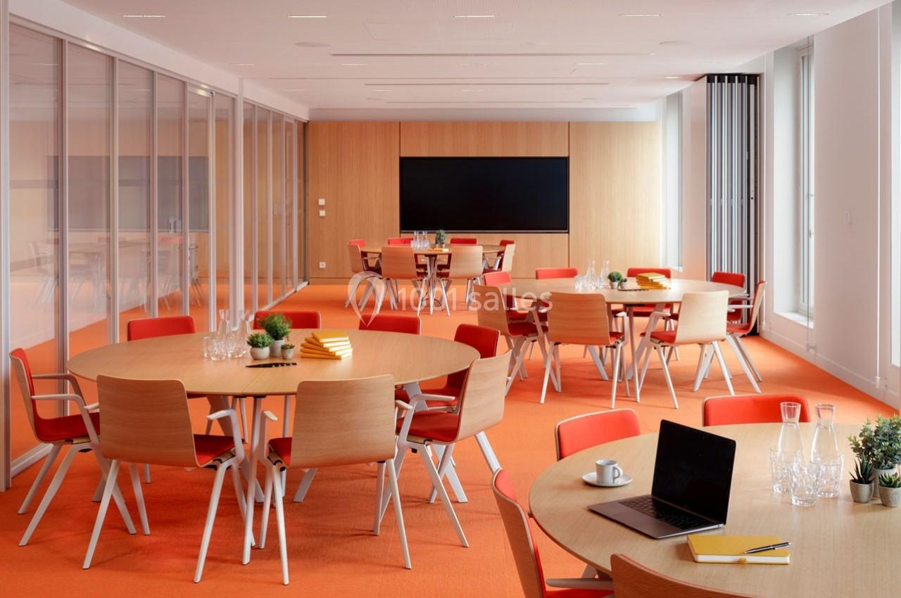 Location salle Paris 9 (Paris) - Pathé Palace  #4 Salle de réunion lumineuse avec tables rondes, chaises orange, écran noir et éléments de décoration modernes.