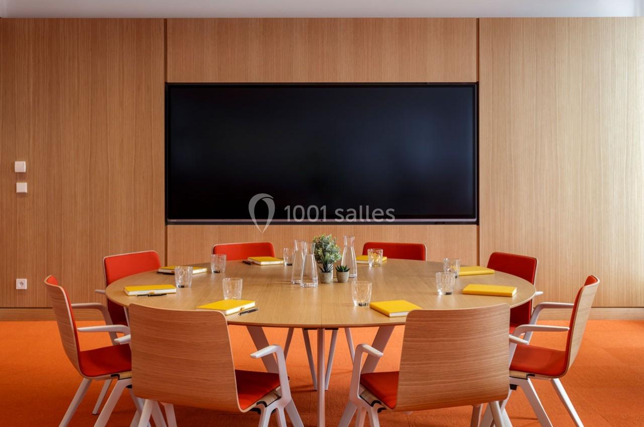 Location salle Paris 9 (Paris) - Pathé Palace  #6 Salle de réunion avec table ronde en bois, chaises rouges, écran mural noir et fournitures de bureau disposées.