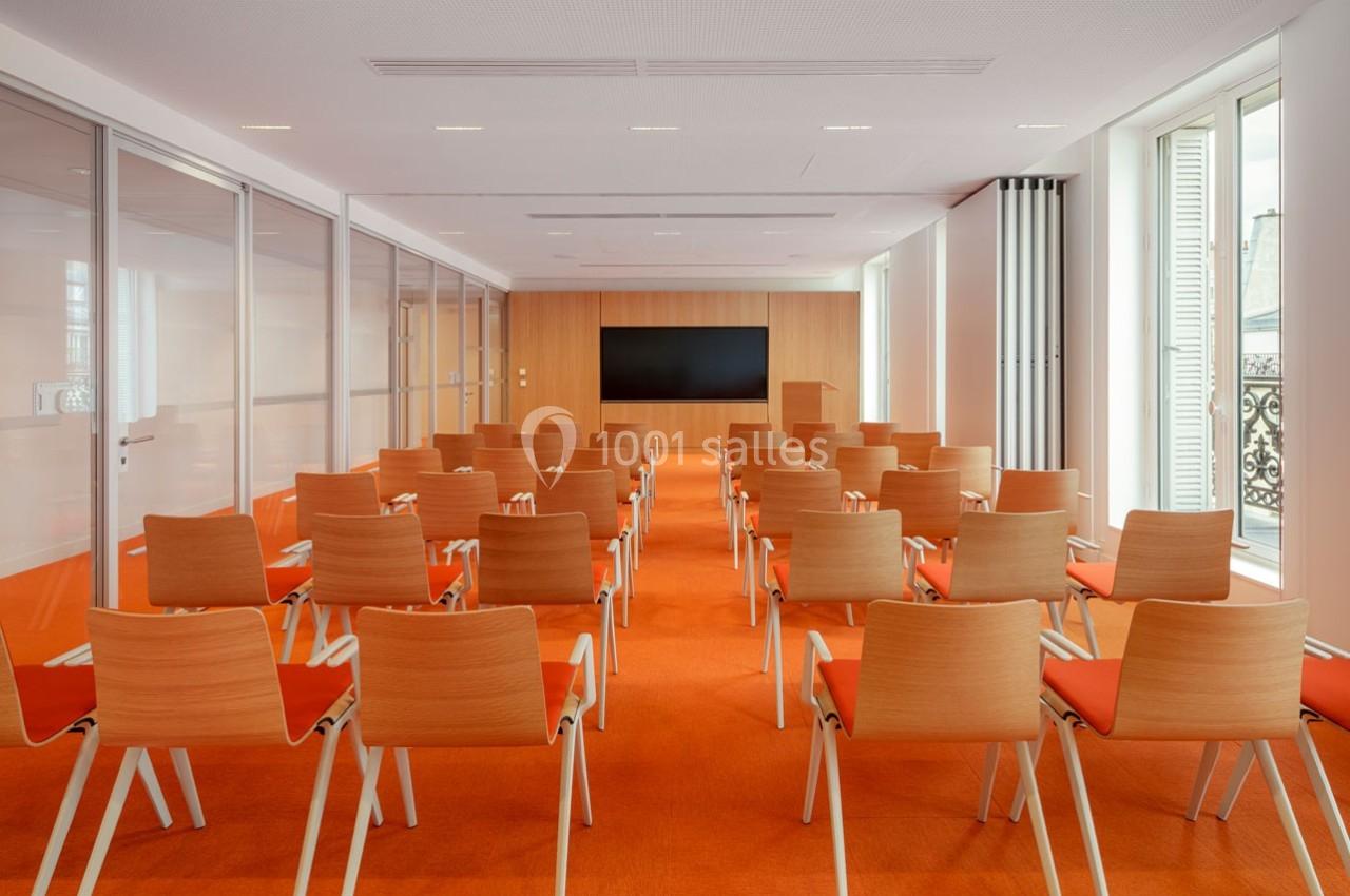 Location salle Paris 9 (Paris) - Pathé Palace  #7 Salle de conférence lumineuse avec des rangées de chaises en bois et un écran noir fixé sur un mur en bois clair.