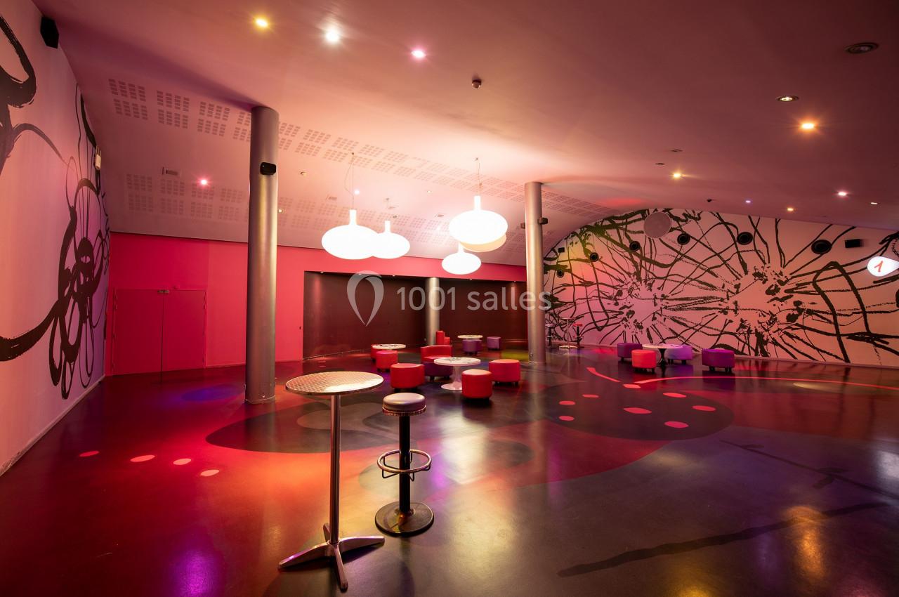 Location salle Paris 15 (Paris) - Pathé Aquaboulevard #6 Salle moderne avec éclairage coloré, murs décorés de motifs abstraits, tables hautes et sièges dispersés.