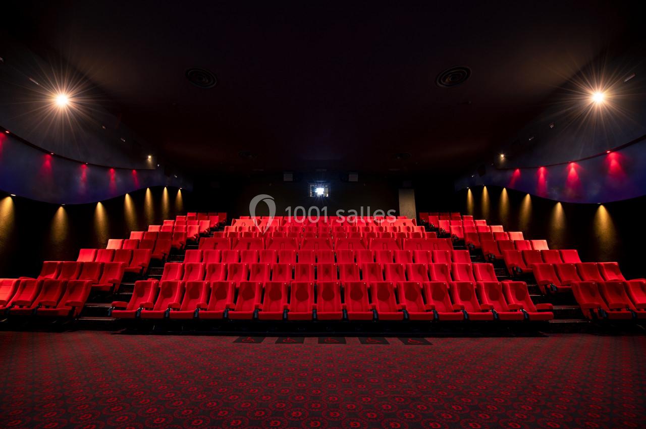 Location salle Paris 15 (Paris) - Pathé Aquaboulevard #7 Salle de cinéma vide avec des rangées de sièges rouges et un écran blanc au fond, éclairée par des lumières tamisées.