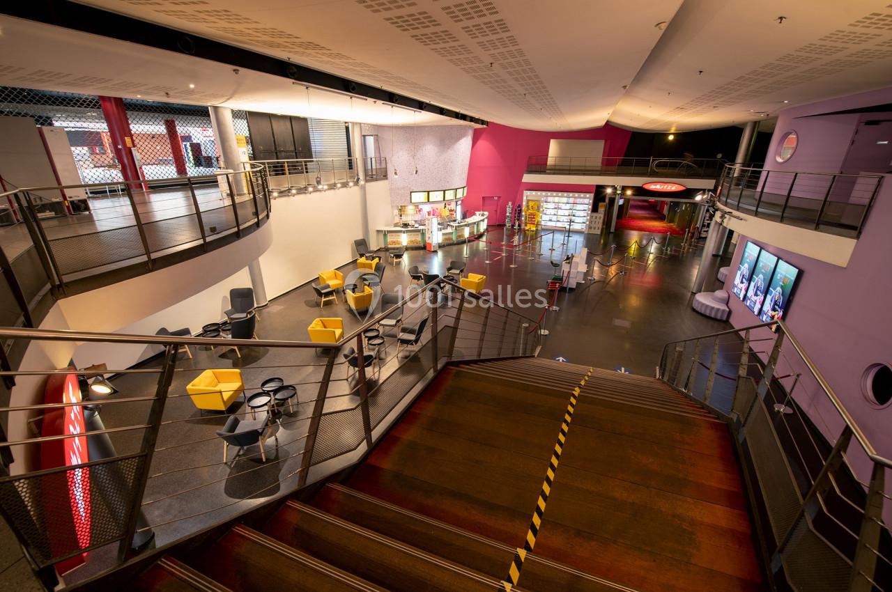 Location salle Paris 15 (Paris) - Pathé Aquaboulevard #11 Vue intérieure d'un espace public moderne avec escalier central, sièges colorés et comptoirs de restauration.