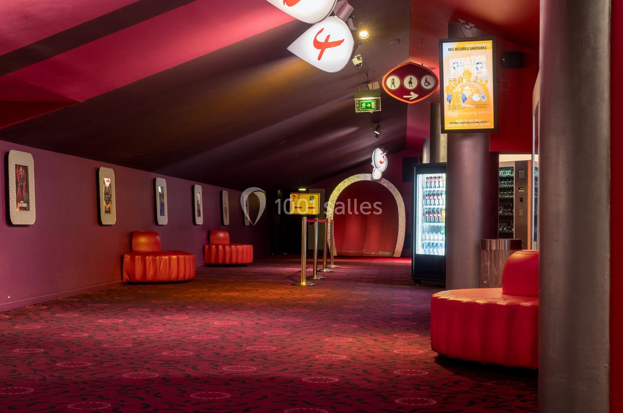 Location salle Paris 15 (Paris) - Pathé Aquaboulevard #14 Couloir d'un cinéma avec moquette rouge, sièges arrondis, distributeurs automatiques et signalétique lumineuse.