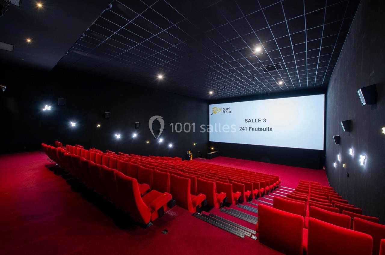 Salle de cinéma vide avec des fauteuils rouges, écran blanc affichant ’Salle 3 - 241 fauteuils’, éclairage tamisé.