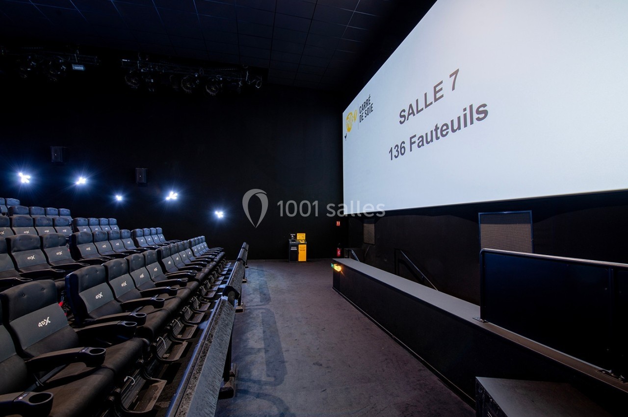Salle de cinéma moderne avec rangées de sièges noirs, grand écran affichant ’Salle 7, 136 fauteuils’.