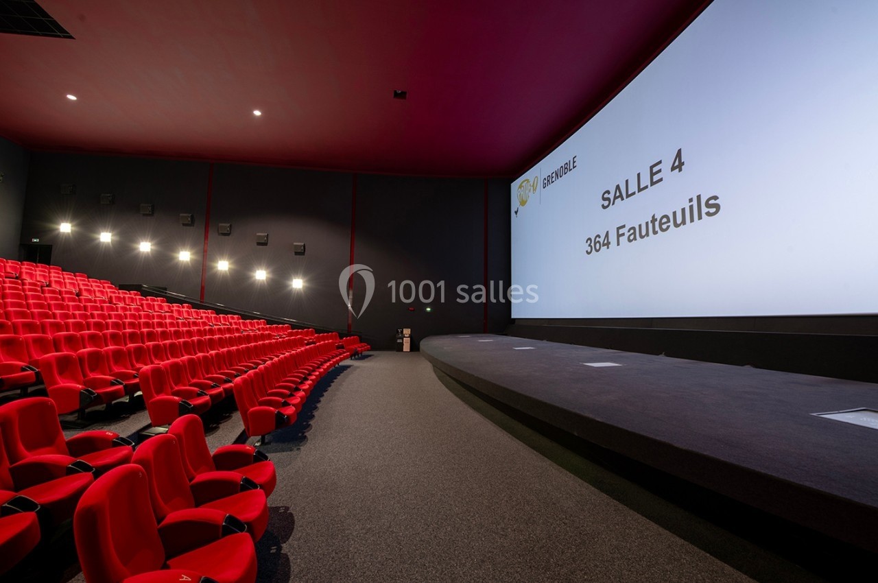 Salle de cinéma vide avec des fauteuils rouges, un grand écran affichant ’Salle 4, 364 fauteuils’ et un éclairage tamisé.