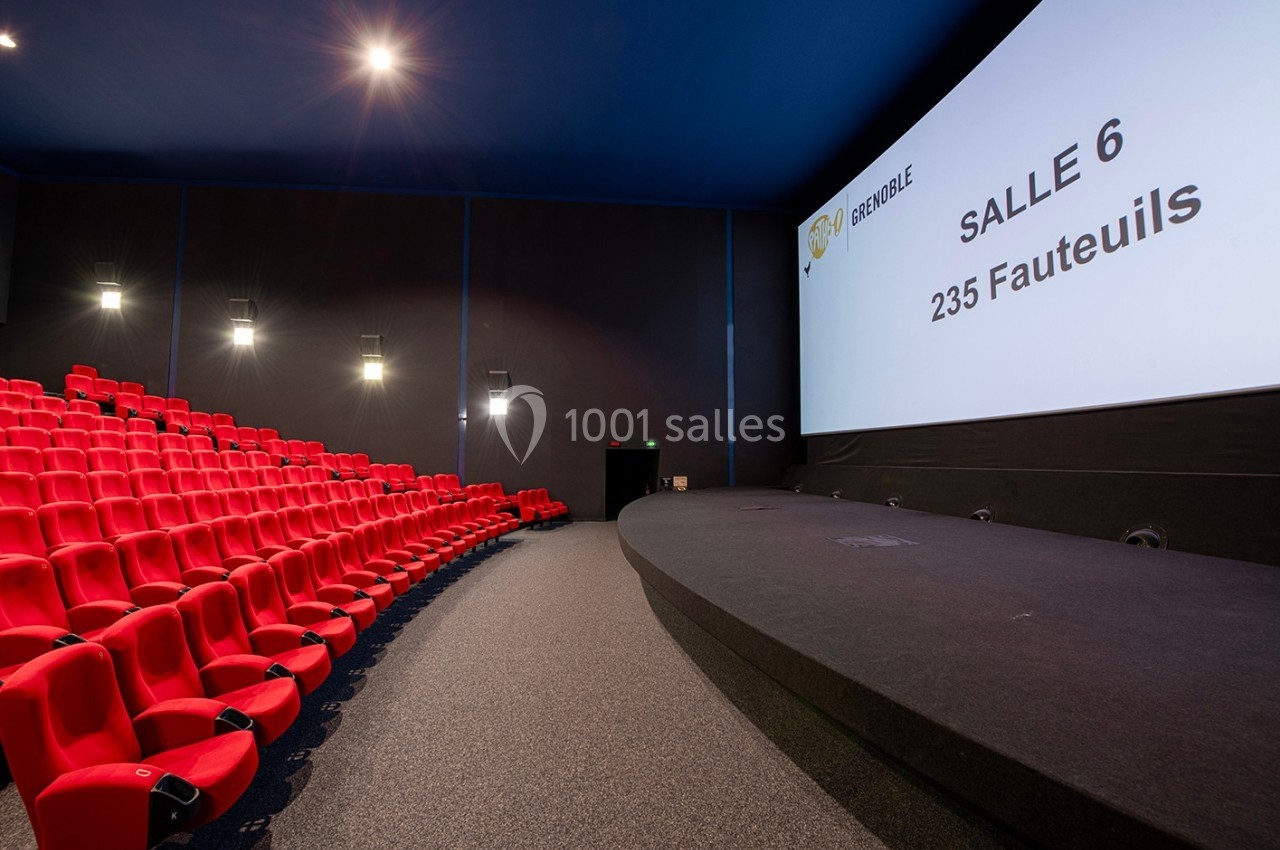 Salle de cinéma moderne avec rangées de fauteuils rouges et grand écran affichant ’Salle 6, 235 fauteuils’.