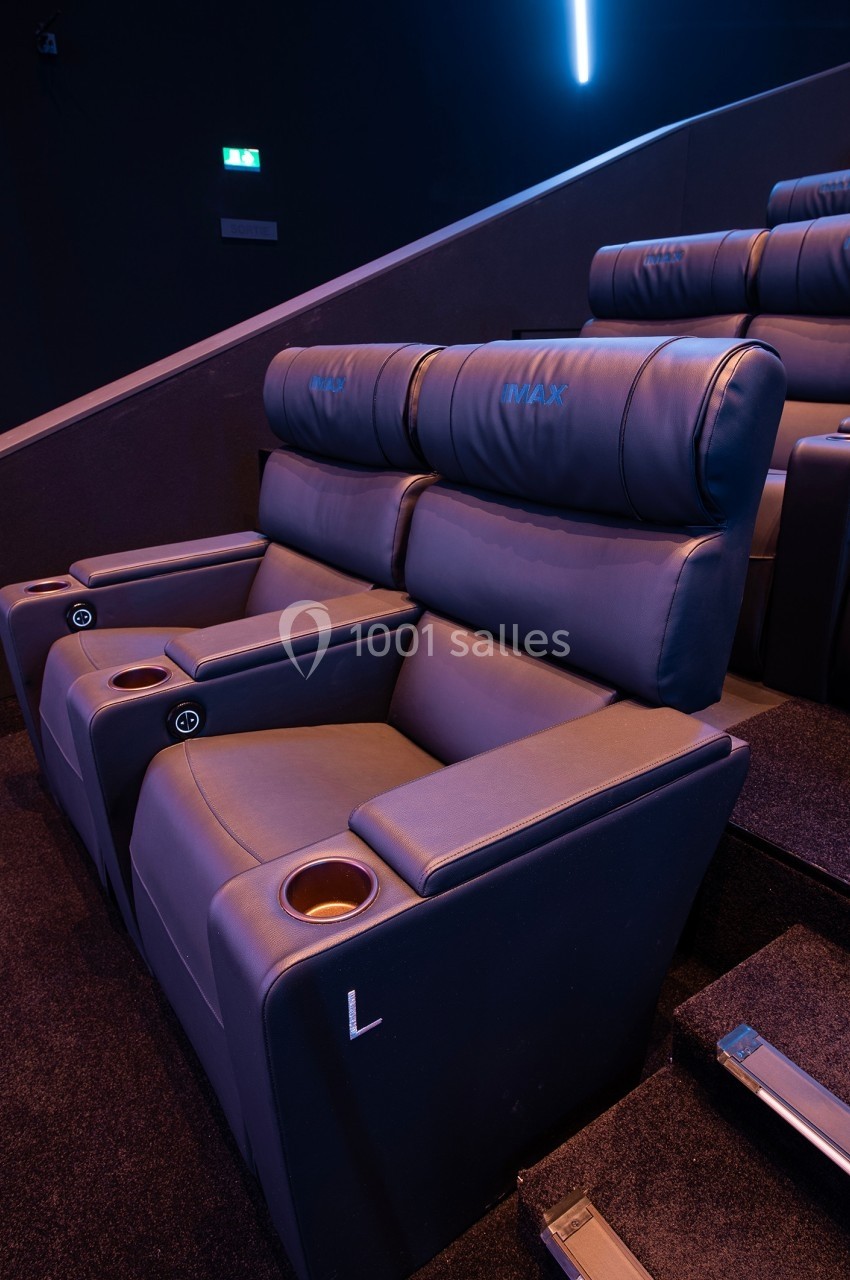 Fauteuils de cinéma en cuir bleu avec porte-gobelets intégrés, disposés dans une salle sombre.