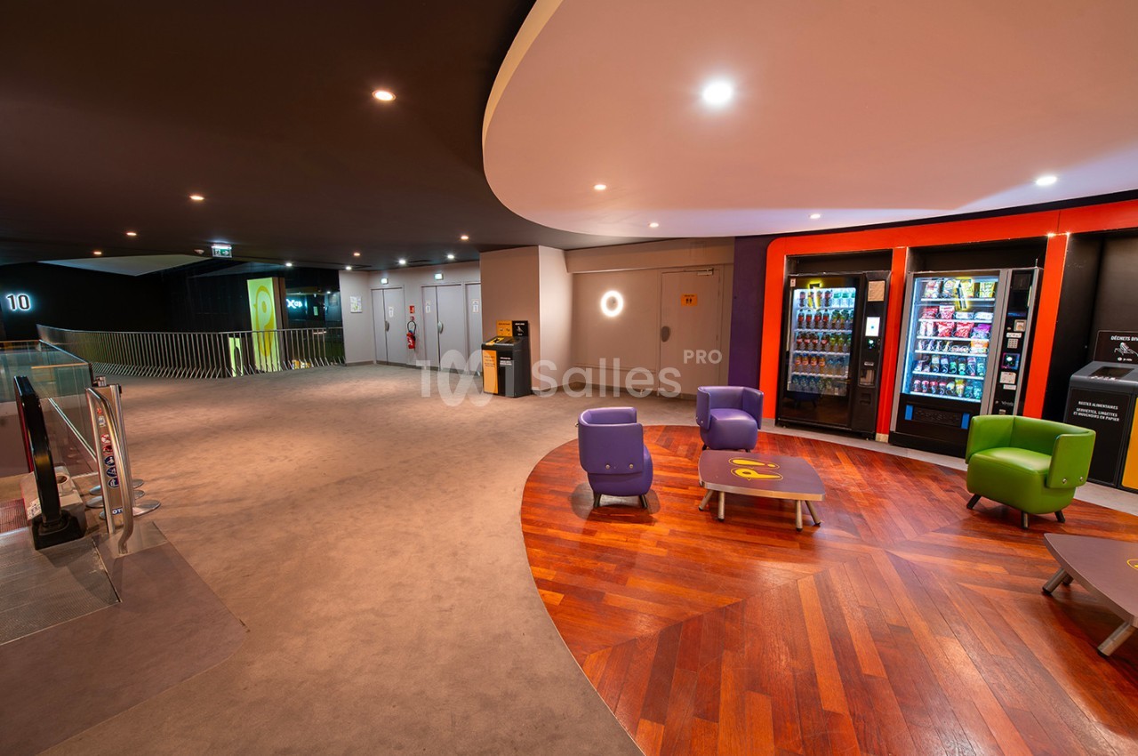 Espace d'attente moderne avec fauteuils colorés, sol en bois et moquette, et distributeurs automatiques en arrière-plan.