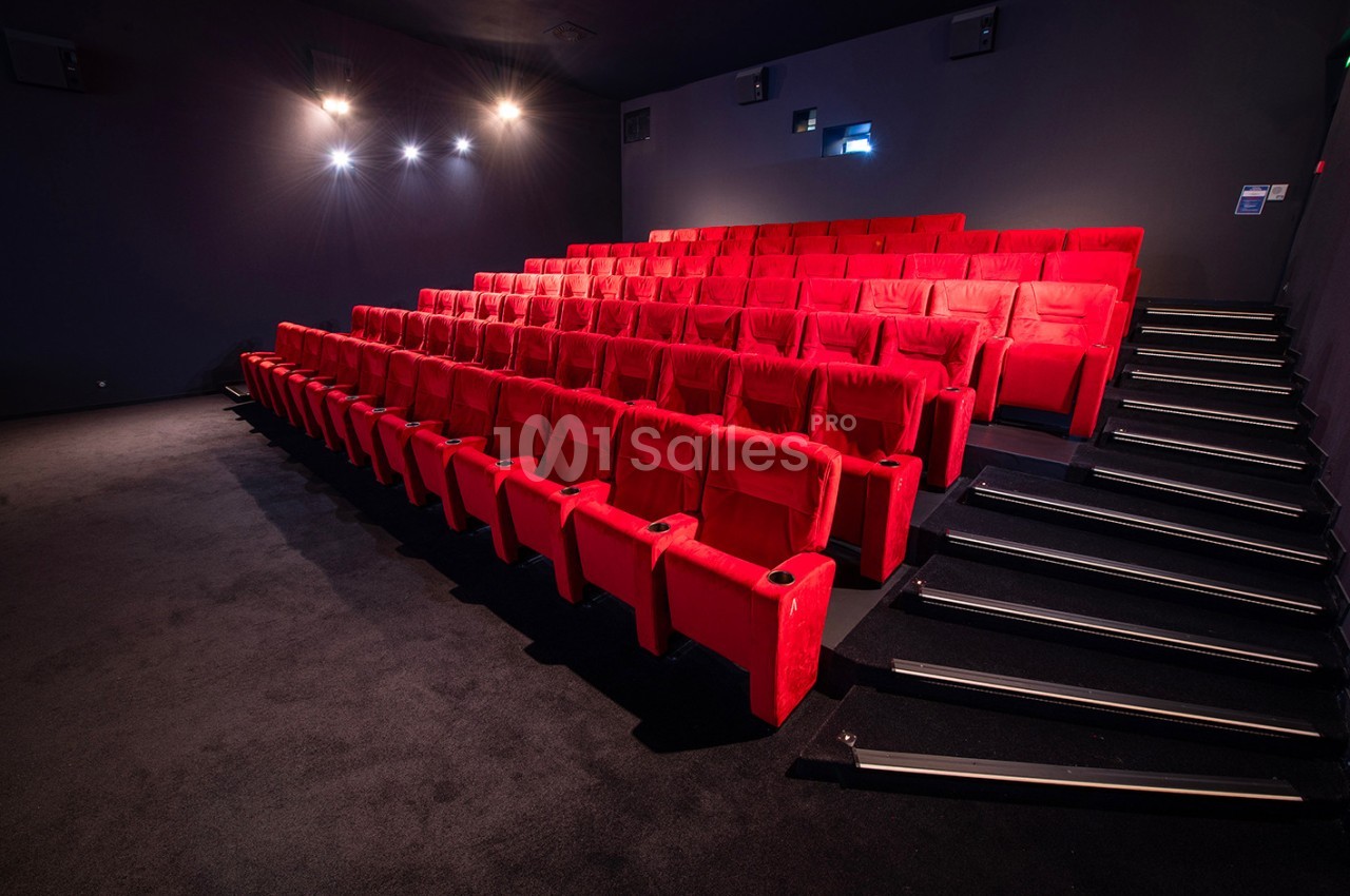Salle de cinéma vide avec des rangées de fauteuils rouges et un éclairage tamisé.