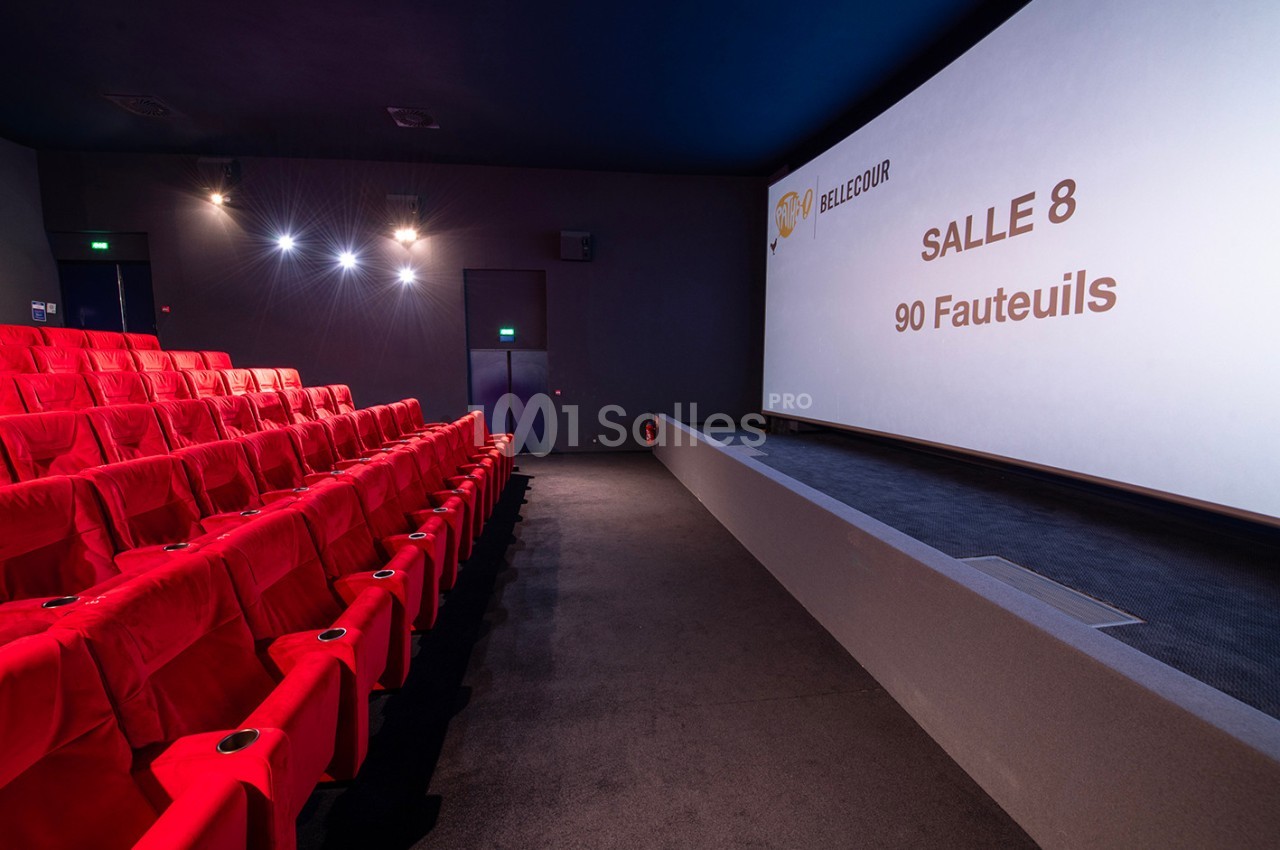 Salle de cinéma avec des fauteuils rouges, un écran affichant ’Salle 8, 90 fauteuils’ et un éclairage tamisé.