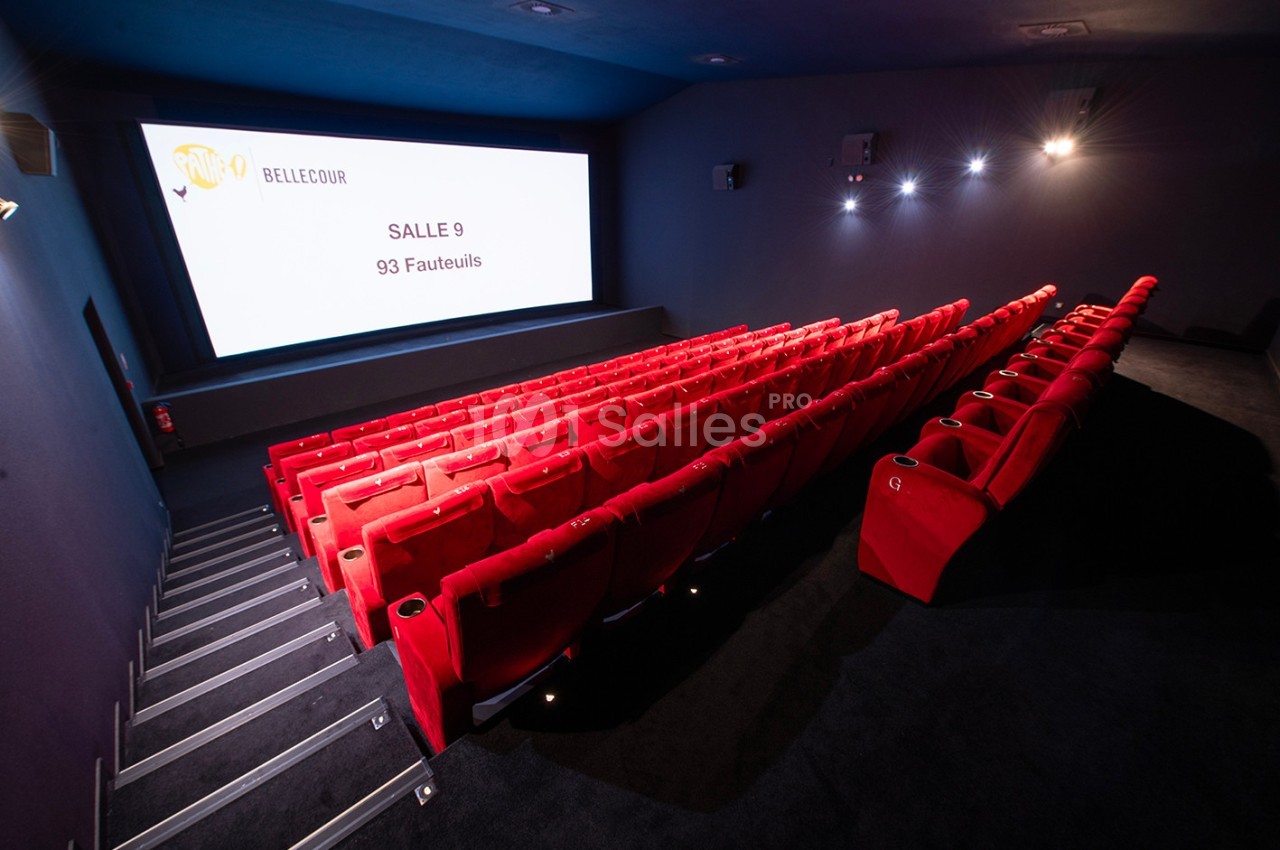 Salle de cinéma vide avec rangées de sièges rouges et un écran affichant ’Salle 9, 93 fauteuils’.