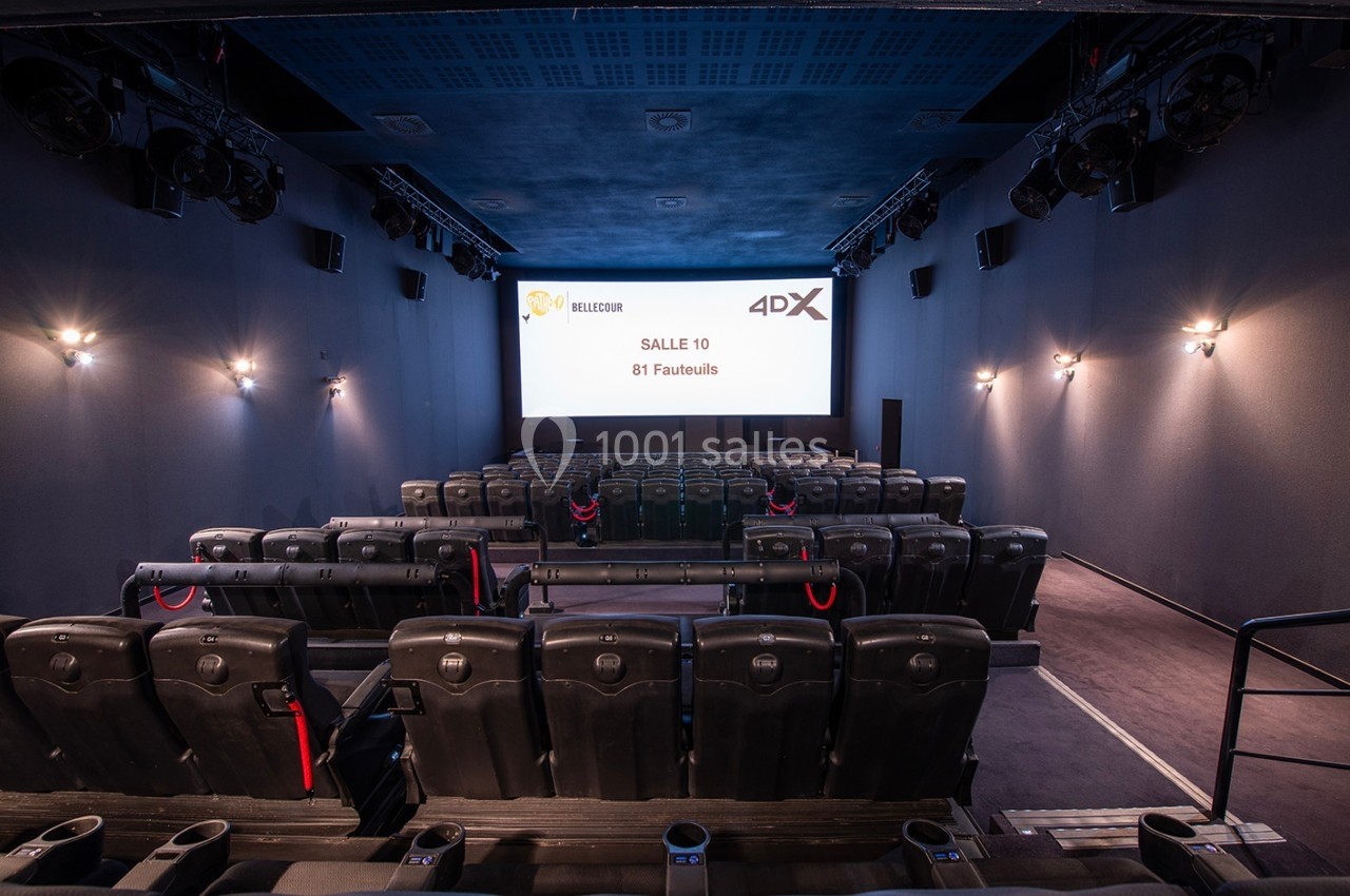 Salle de cinéma vide avec sièges noirs, écran affichant ’Salle 10, 81 fauteuils’ et éclairage mural tamisé.