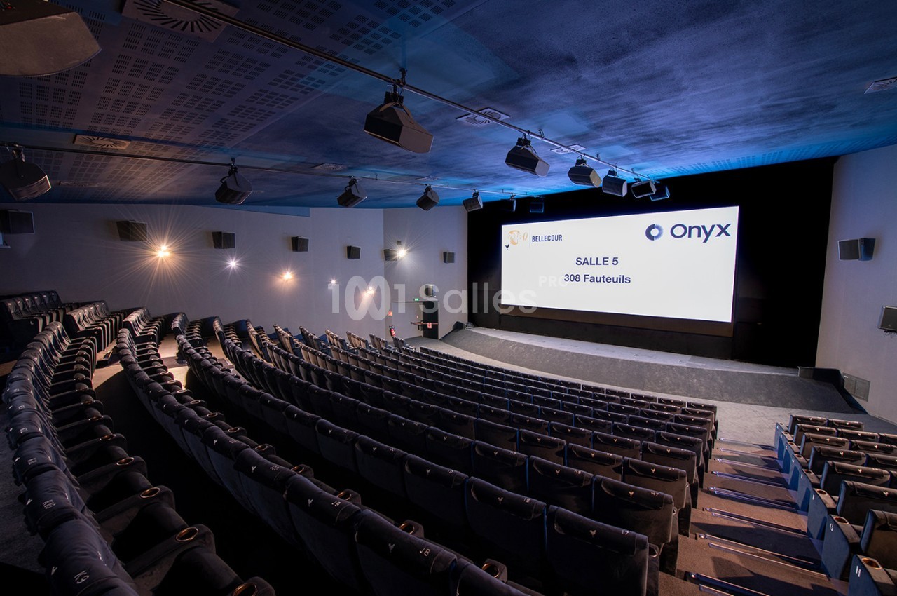 Salle de cinéma moderne avec écran large, sièges inclinés et éclairage tamisé, affichant ’Salle 5 - 308 Fauteuils’.