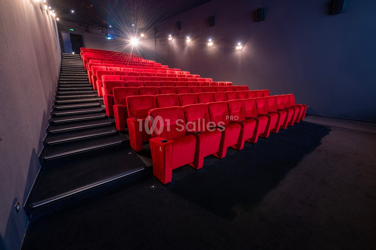 Salle de cinéma vide avec des rangées de fauteuils rouges et un éclairage tamisé.