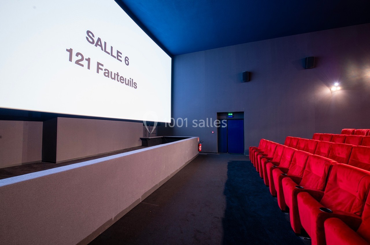 Salle de cinéma vide avec écran affichant ’Salle 6 - 121 fauteuils’ et rangées de sièges rouges.