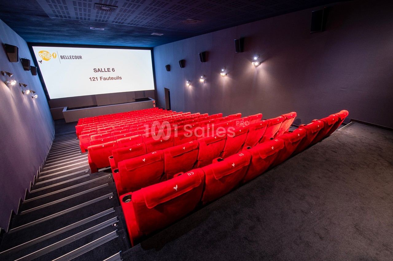 Salle de cinéma vide avec des rangées de fauteuils rouges et un écran affichant ’Salle 6 - 121 Fauteuils’.