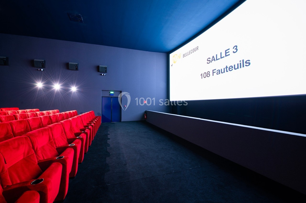 Salle de cinéma moderne avec des fauteuils rouges, un écran allumé affichant des informations et une sortie au fond.