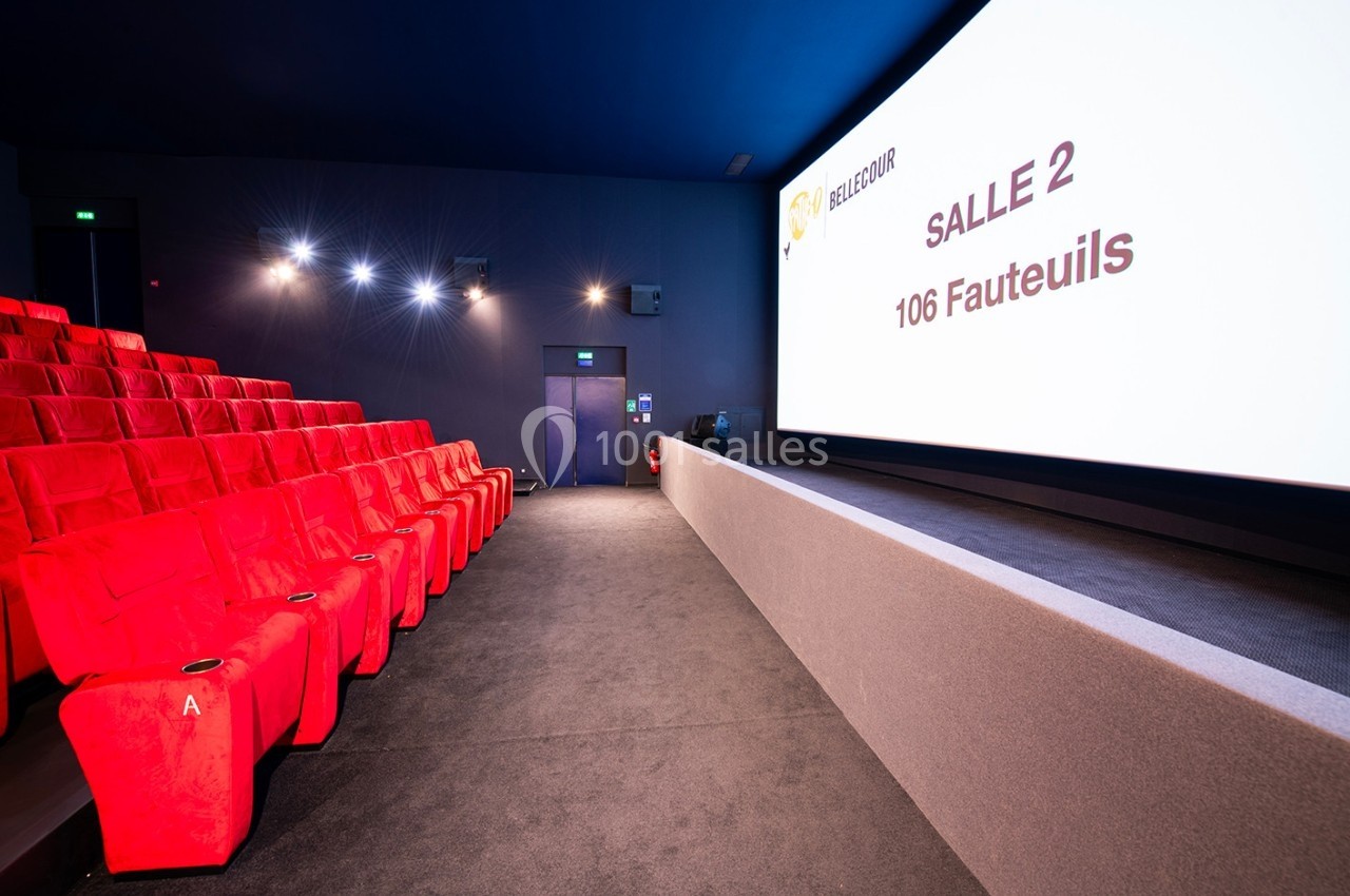 Salle de cinéma vide avec des sièges rouges, un écran affichant ’Salle 2, 106 fauteuils’ et un éclairage tamisé.