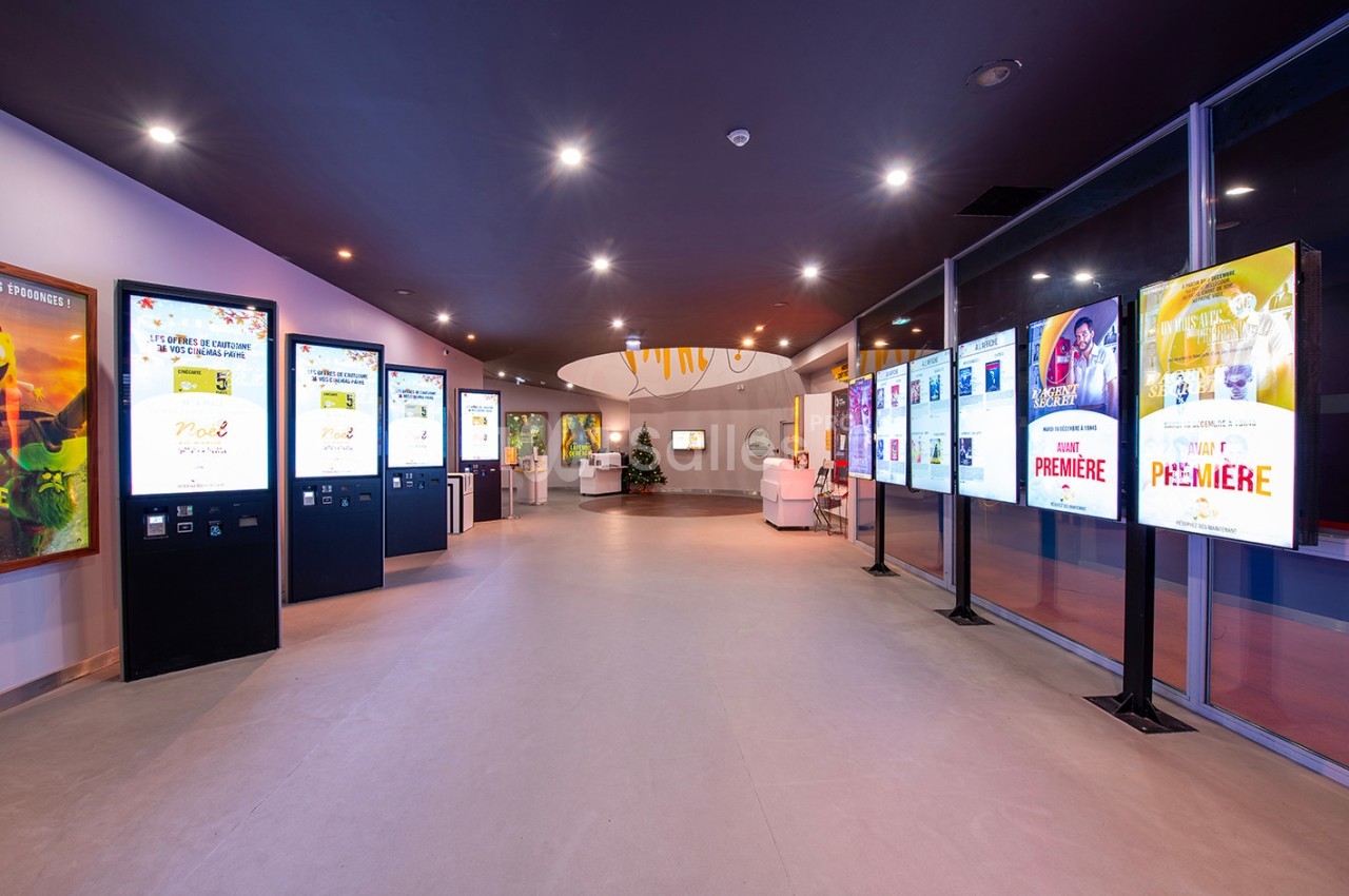 Vue d'un hall moderne avec des écrans numériques affichant des affiches et des informations, éclairage lumineux.