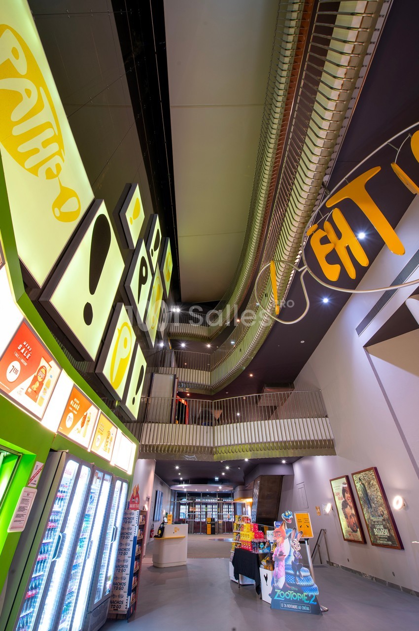 Hall de cinéma moderne avec affiches lumineuses, distributeurs automatiques et escalier menant à l'étage supérieur.