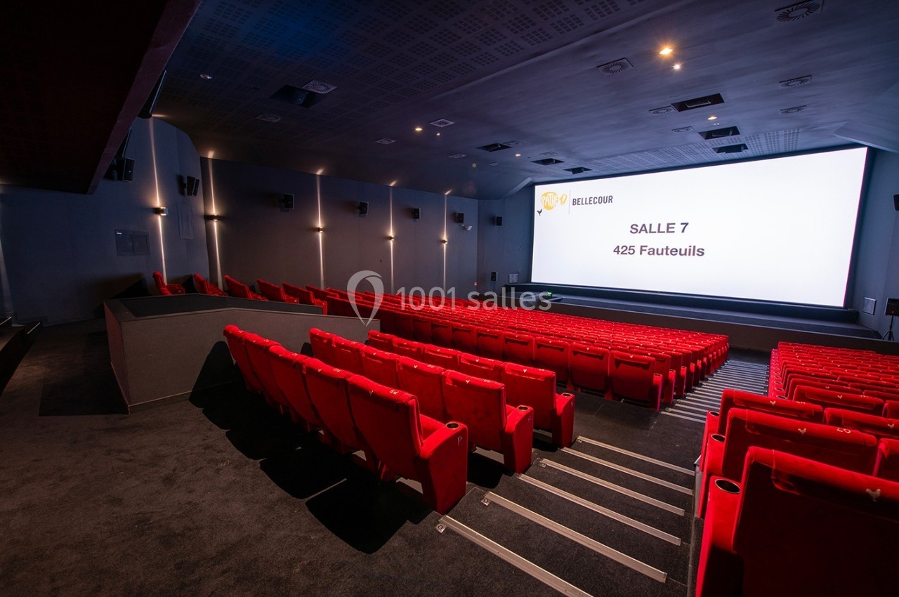 Salle de cinéma moderne avec des rangées de fauteuils rouges et un grand écran affichant ’Salle 7, 425 fauteuils’.