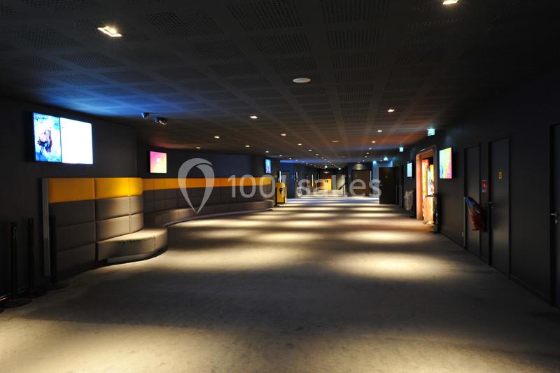 Couloir d'un cinéma moderne avec éclairage tamisé, écrans d'affichage et sièges le long des murs.