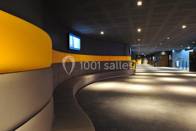 Couloir moderne avec banquette incurvée grise et jaune, éclairage tamisé et écrans muraux.