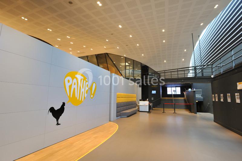 Hall d'entrée moderne avec logo ’Pathé’ sur un mur, comptoir d'accueil et escalier menant à l'étage.