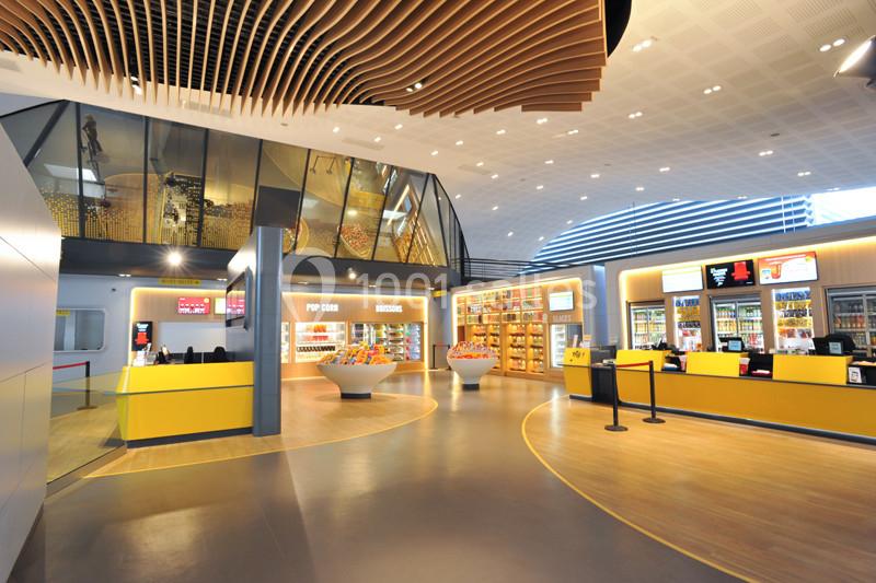 Hall lumineux d'un cinéma avec comptoirs de confiserie, présentoirs de snacks et architecture moderne en bois.