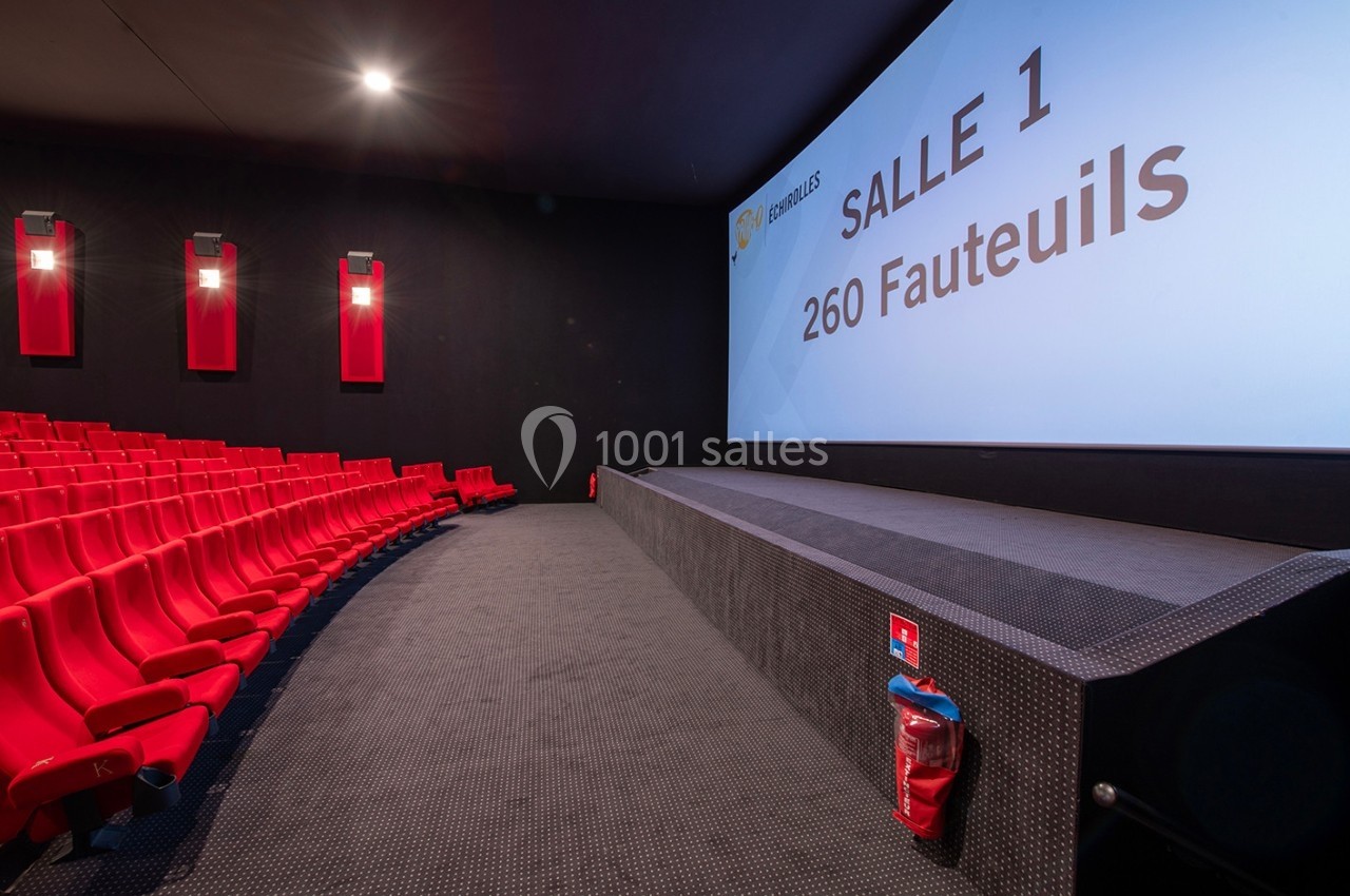 Salle de cinéma moderne avec sièges rouges, écran affichant ’Salle 1 - 260 fauteuils’ et extincteur au premier plan.