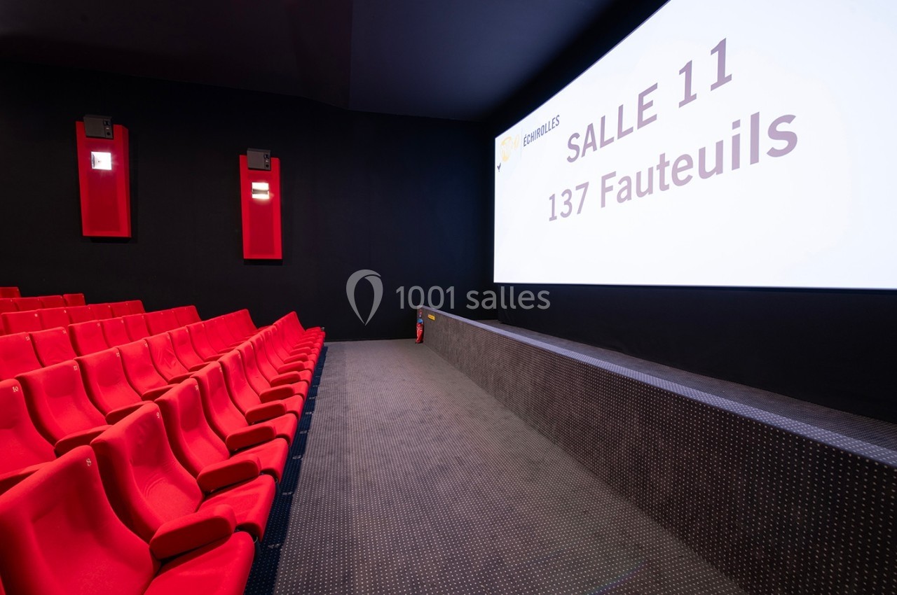 Salle de cinéma vide avec des sièges rouges, un écran affichant ’Salle 11, 137 fauteuils’ et un mur noir.