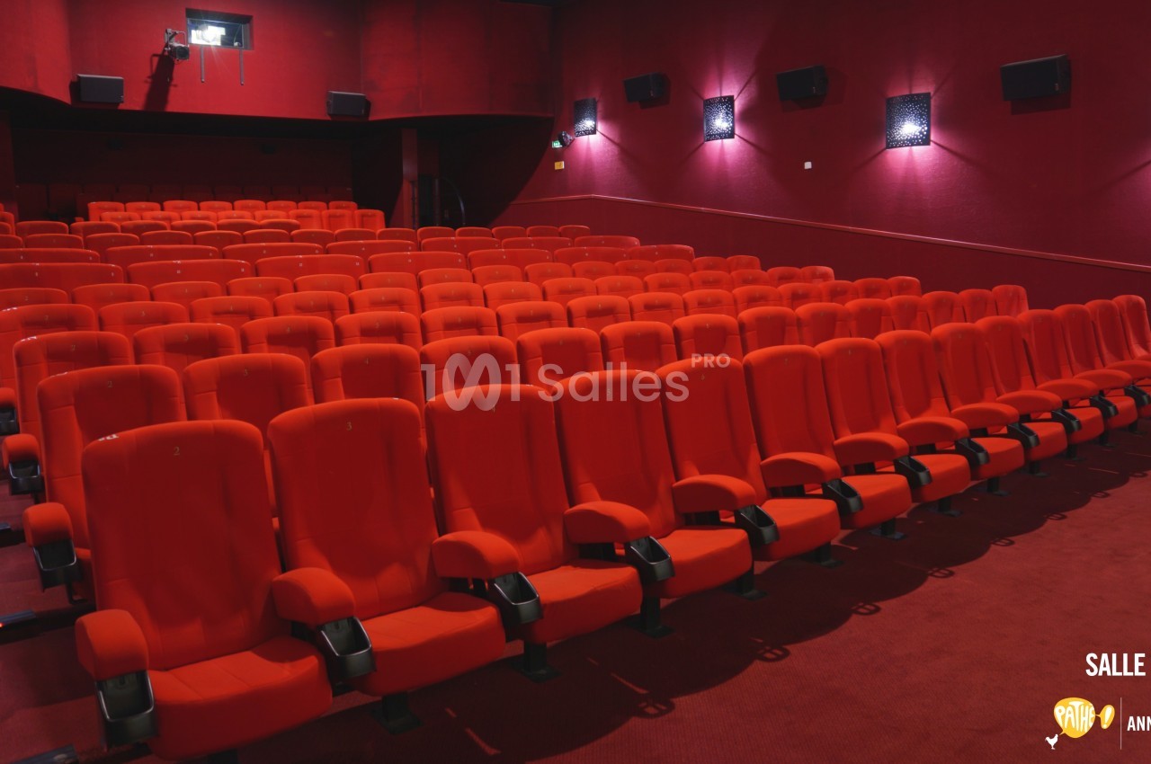 Salle de cinéma vide avec des rangées de fauteuils rouges alignés dans un espace sombre.