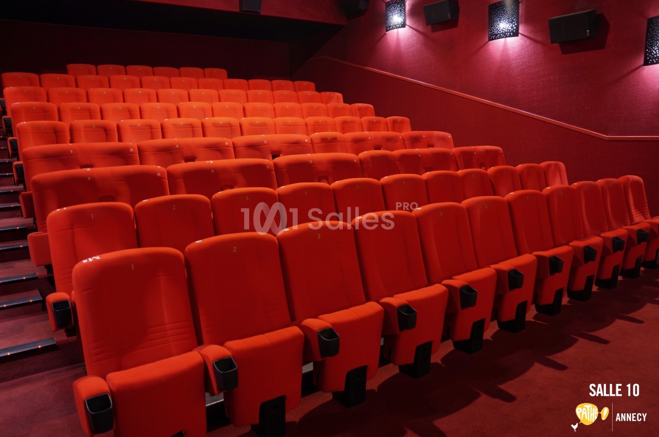 Rangées de sièges rouges alignés dans une salle de cinéma vide, éclairée par une lumière tamisée.