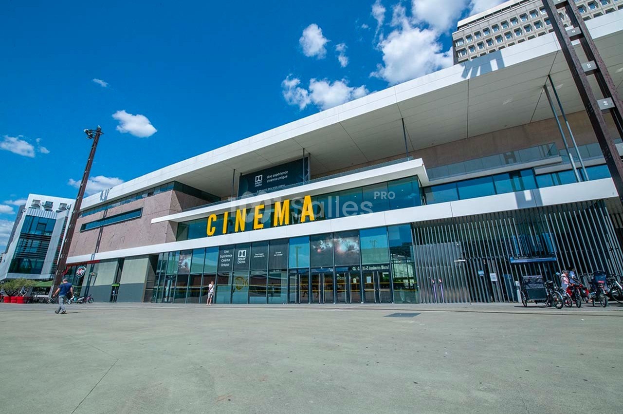 Façade moderne d'un cinéma avec une large entrée vitrée et des lettres jaunes indiquant ’CINEMA’.
