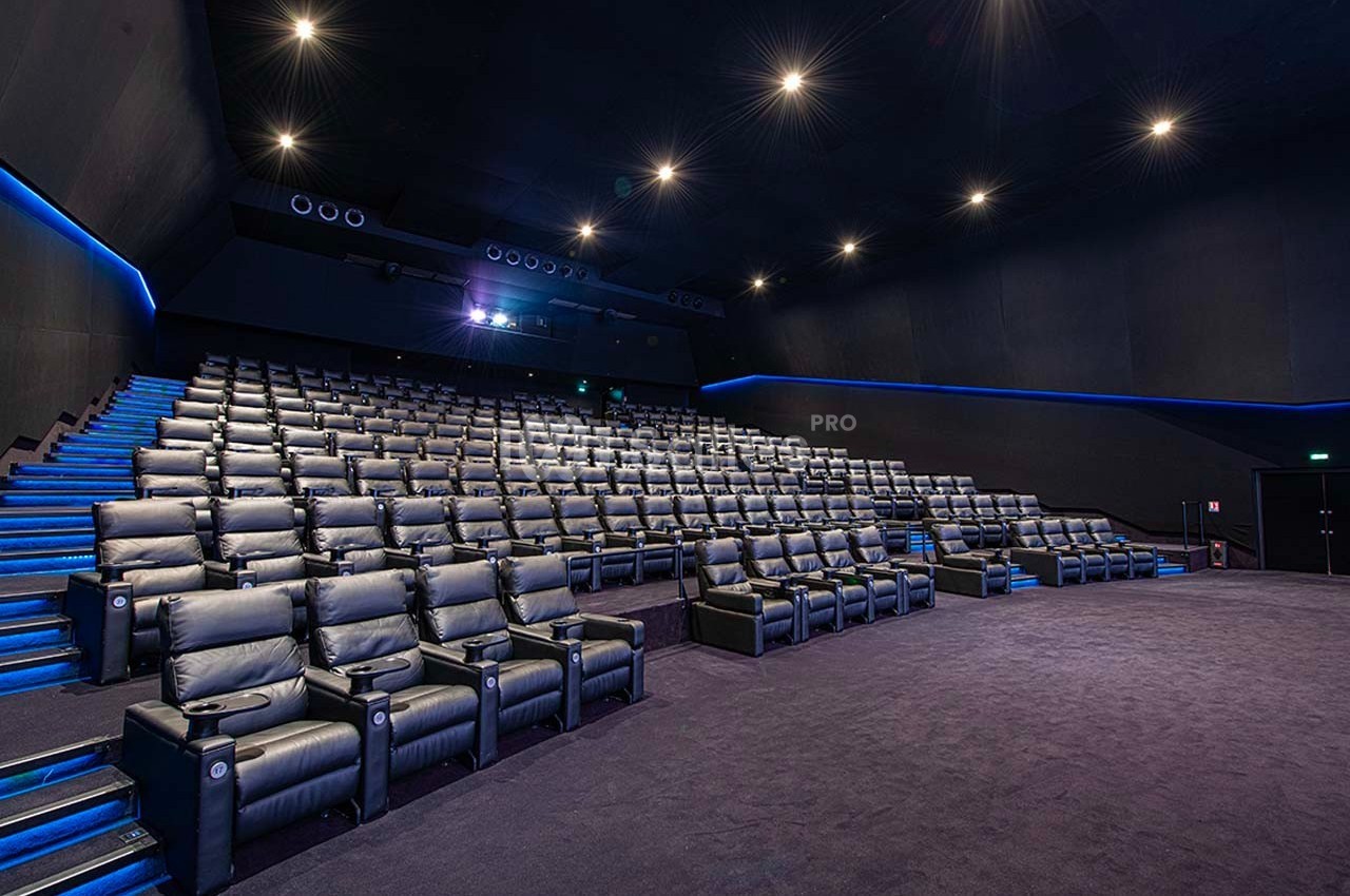 Salle de cinéma vide avec des fauteuils en cuir noir, éclairage tamisé et allées illuminées.