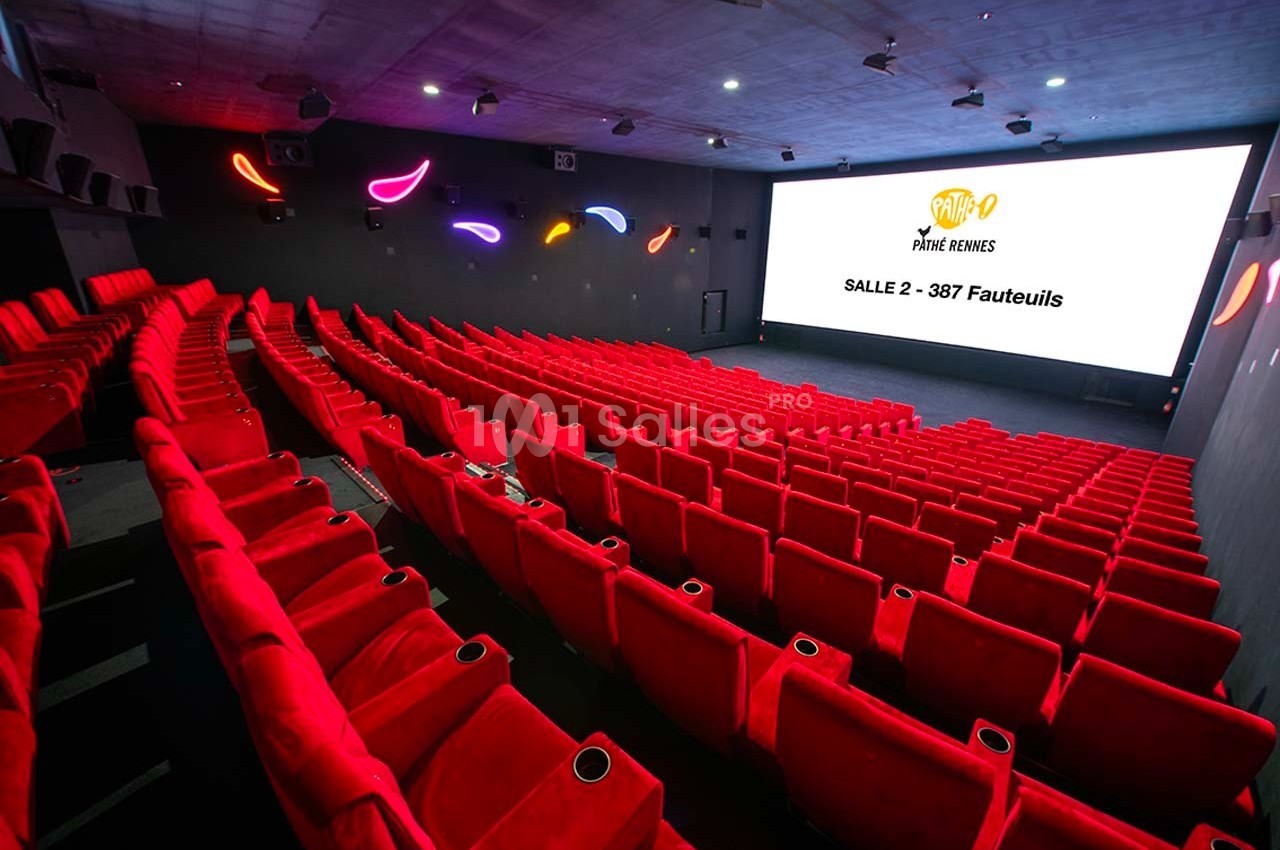 Salle de cinéma moderne avec rangées de fauteuils rouges et écran affichant ’Salle 2 - 387 fauteuils’.