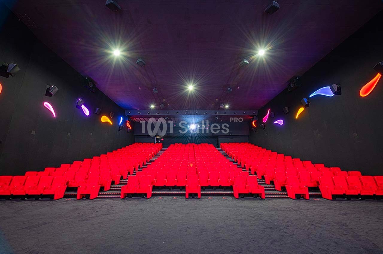 Salle de cinéma vide avec rangées de sièges rouges, éclairage tamisé et décorations lumineuses sur les murs.