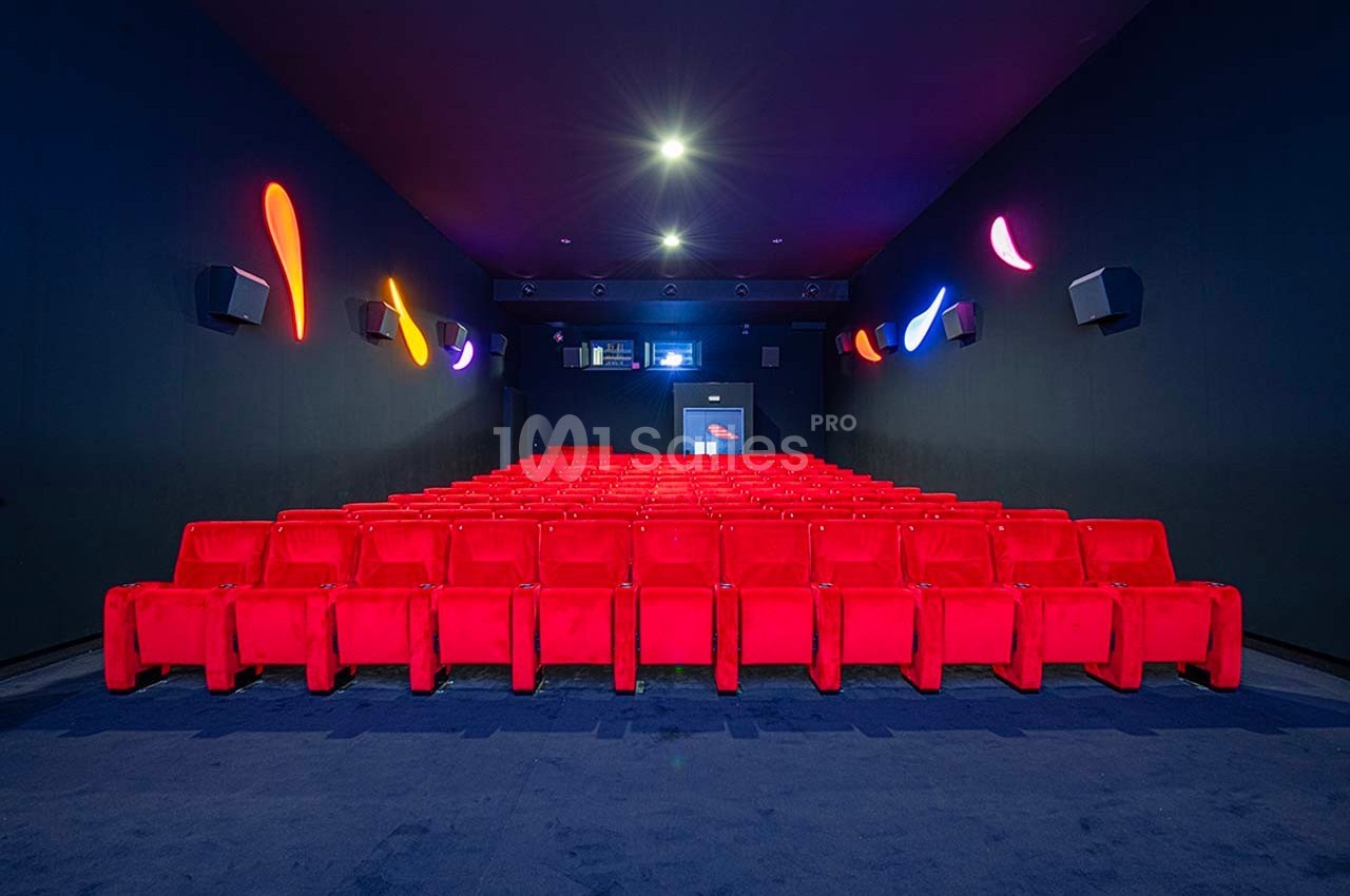 Salle de cinéma vide avec rangées de sièges rouges, murs sombres et éclairage coloré décoratif.